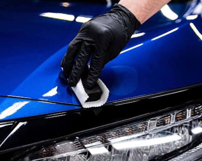 Technician applying ceramic coating on a blue car hood with a foam applicator pad