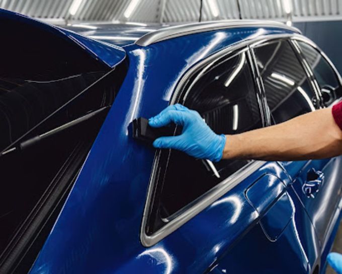 Detailer buffing ceramic coating around the window trim of a dark blue car