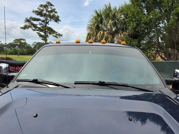 Close-up of a dark truck windshield with orange cab lights showing a clean window tint application