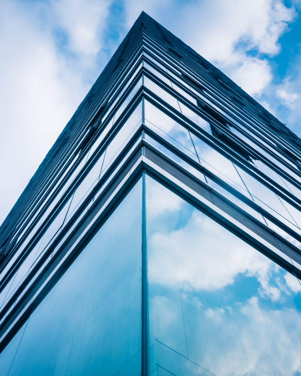 Blue glass skyscraper corner reflecting cloudy sky.