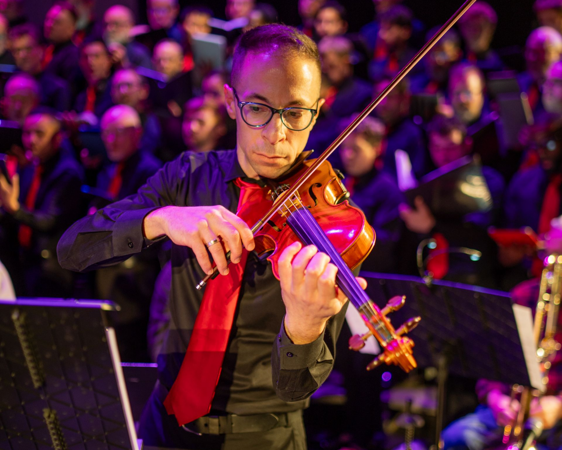 PGMC Violinist in a black shirt and red tie performing on stage under purple lights,