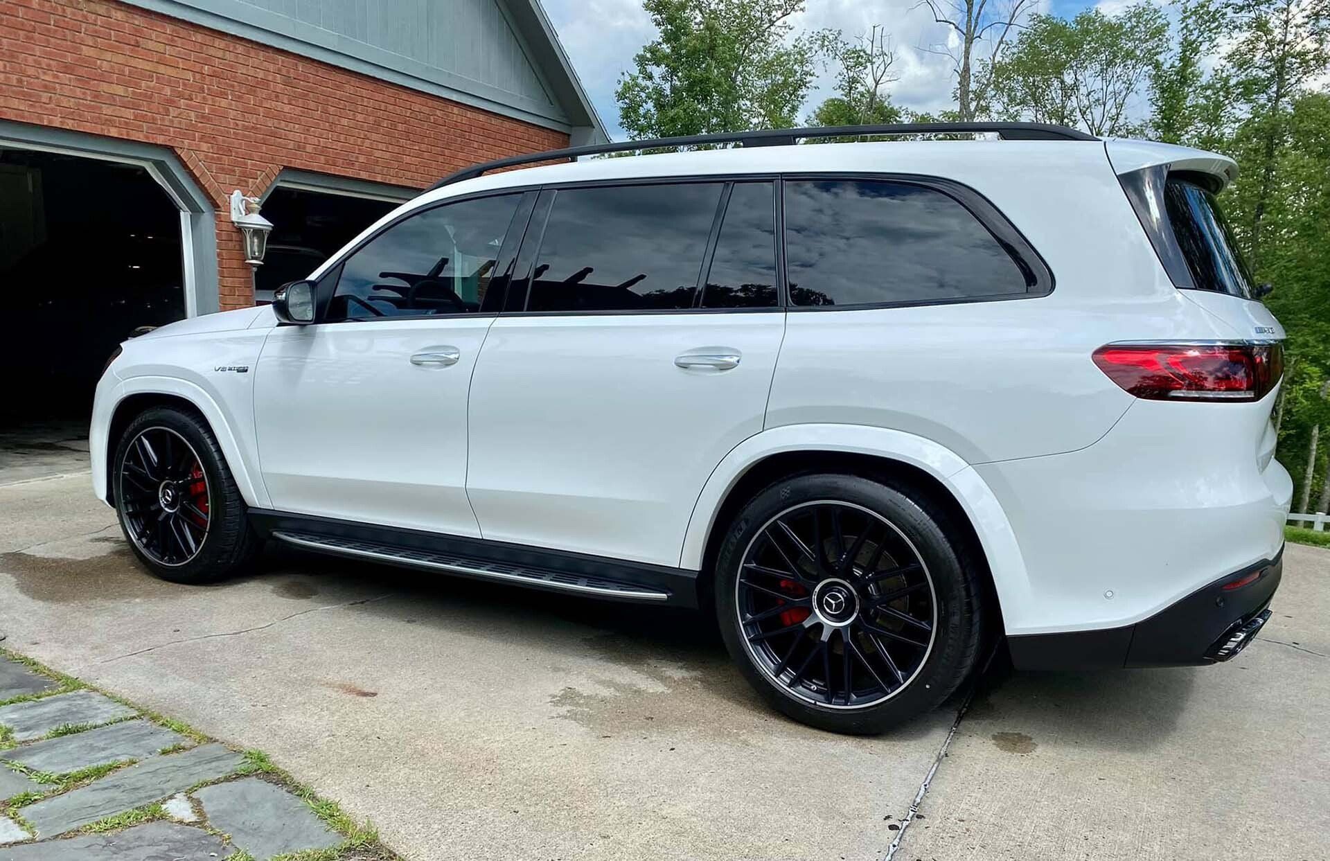 White SUV parked outside a brick building with black tinted windows and black wheels.