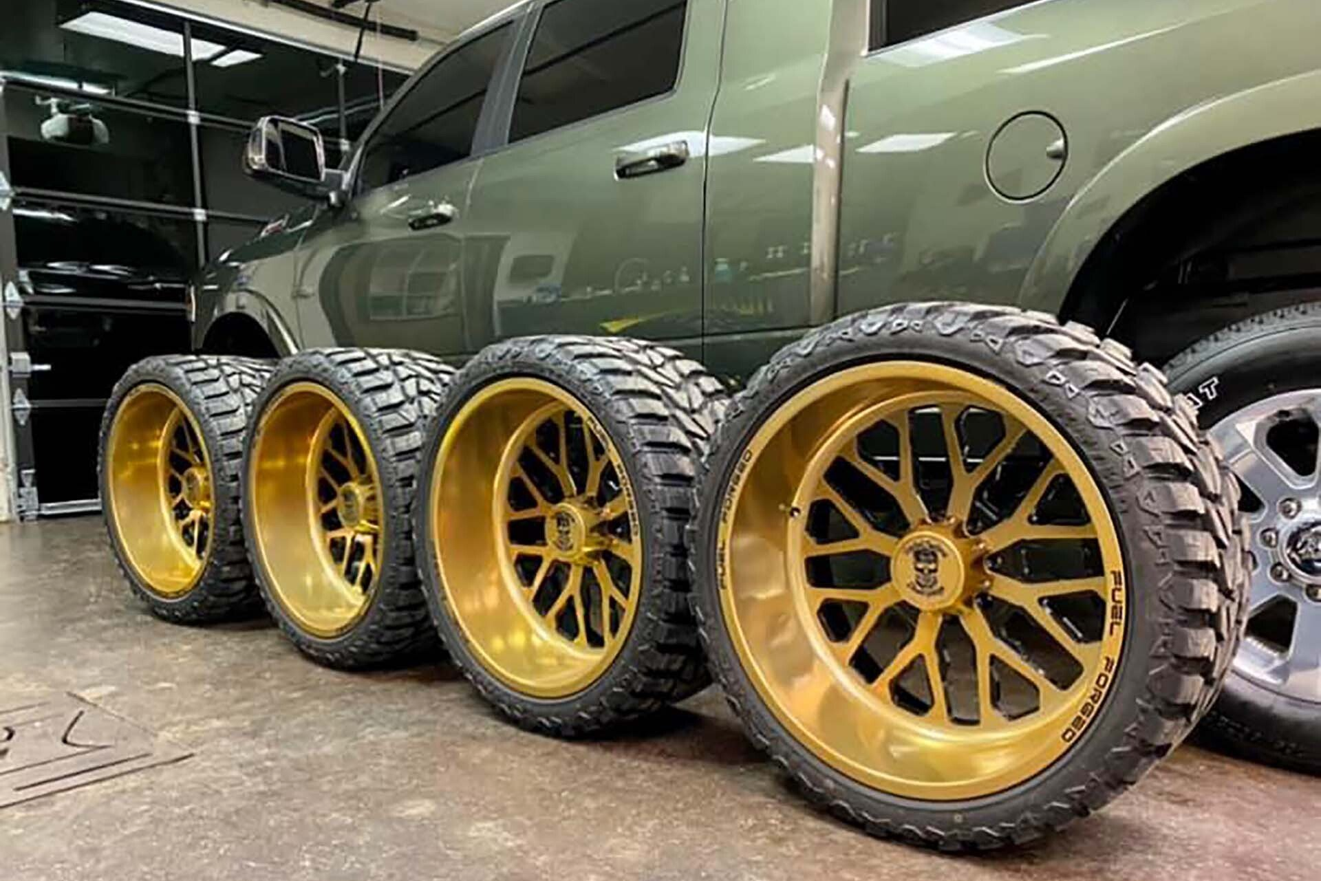 Four gold rims with black tires next to a green pickup truck in a shop.
