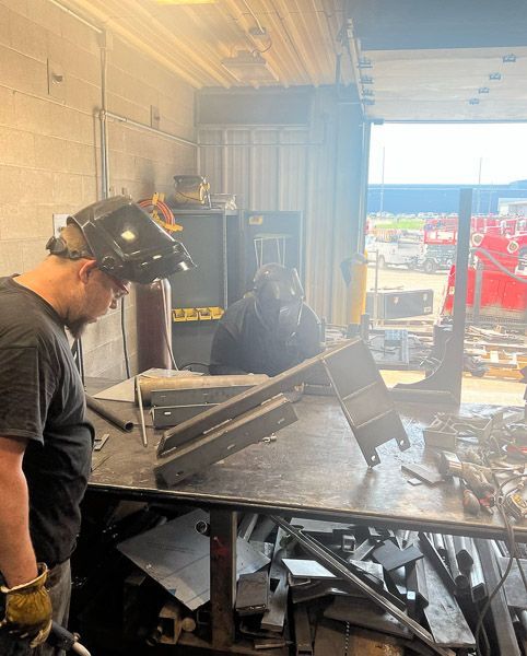 A man wearing a welding helmet is standing in front of a table.