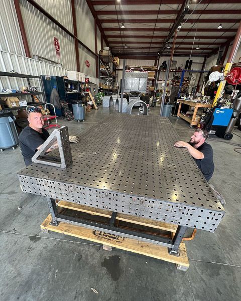 Two men are working on a welding table in a factory.