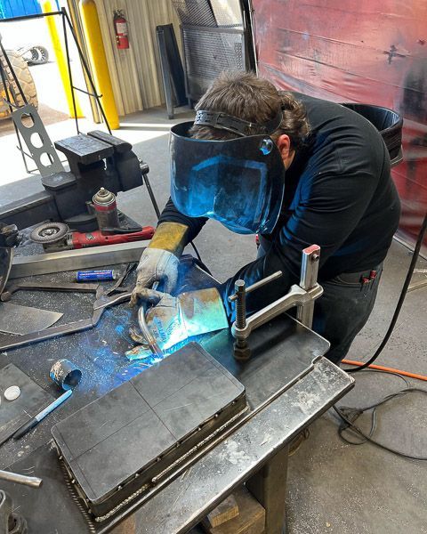 A man wearing a welding mask is welding a piece of metal.