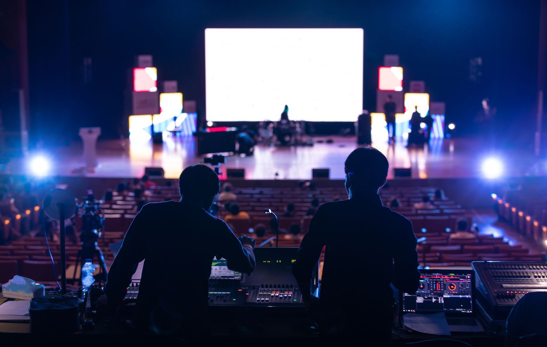Two men are standing in front of a large screen on a stage.