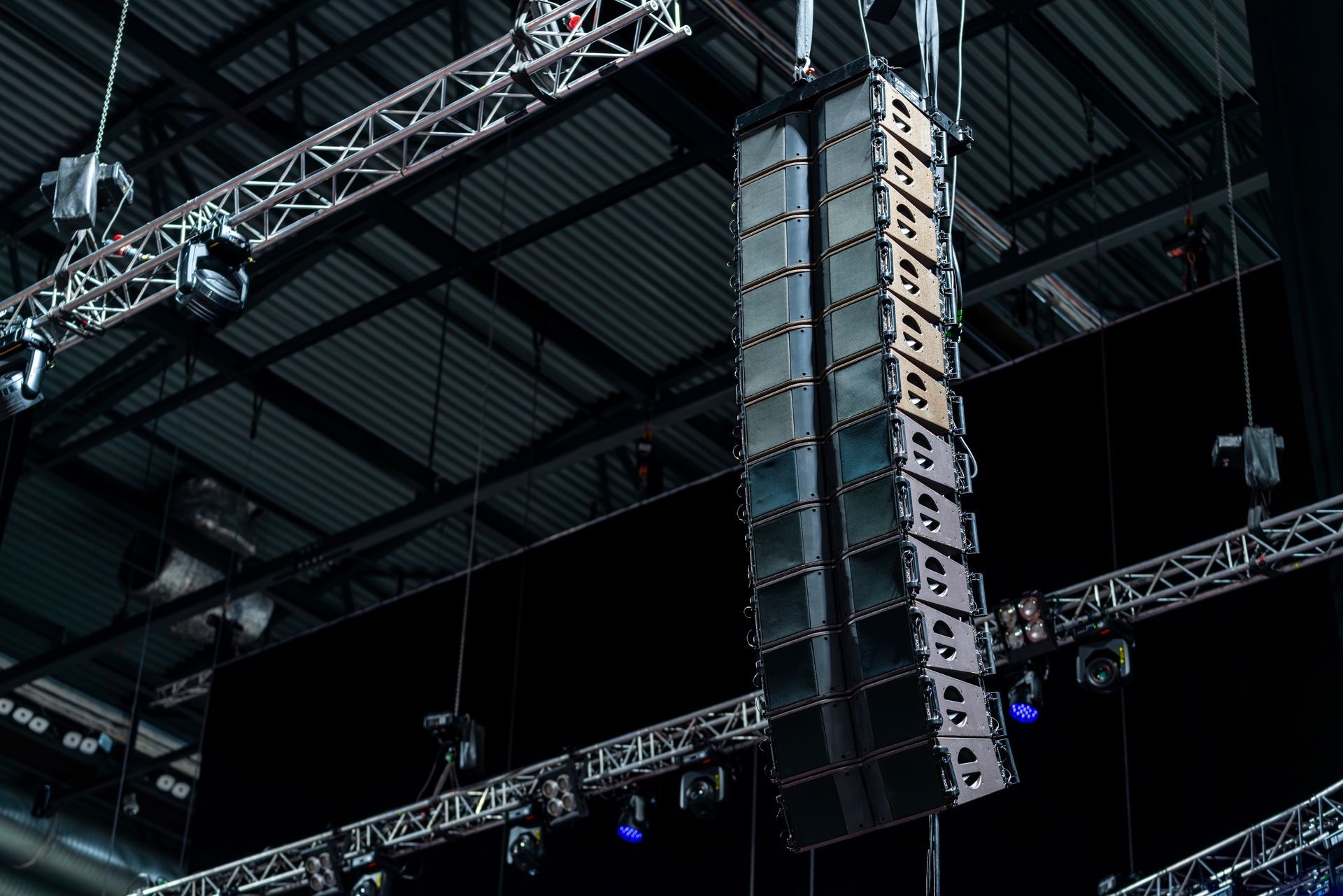 A row of speakers are hanging from the ceiling of a building.