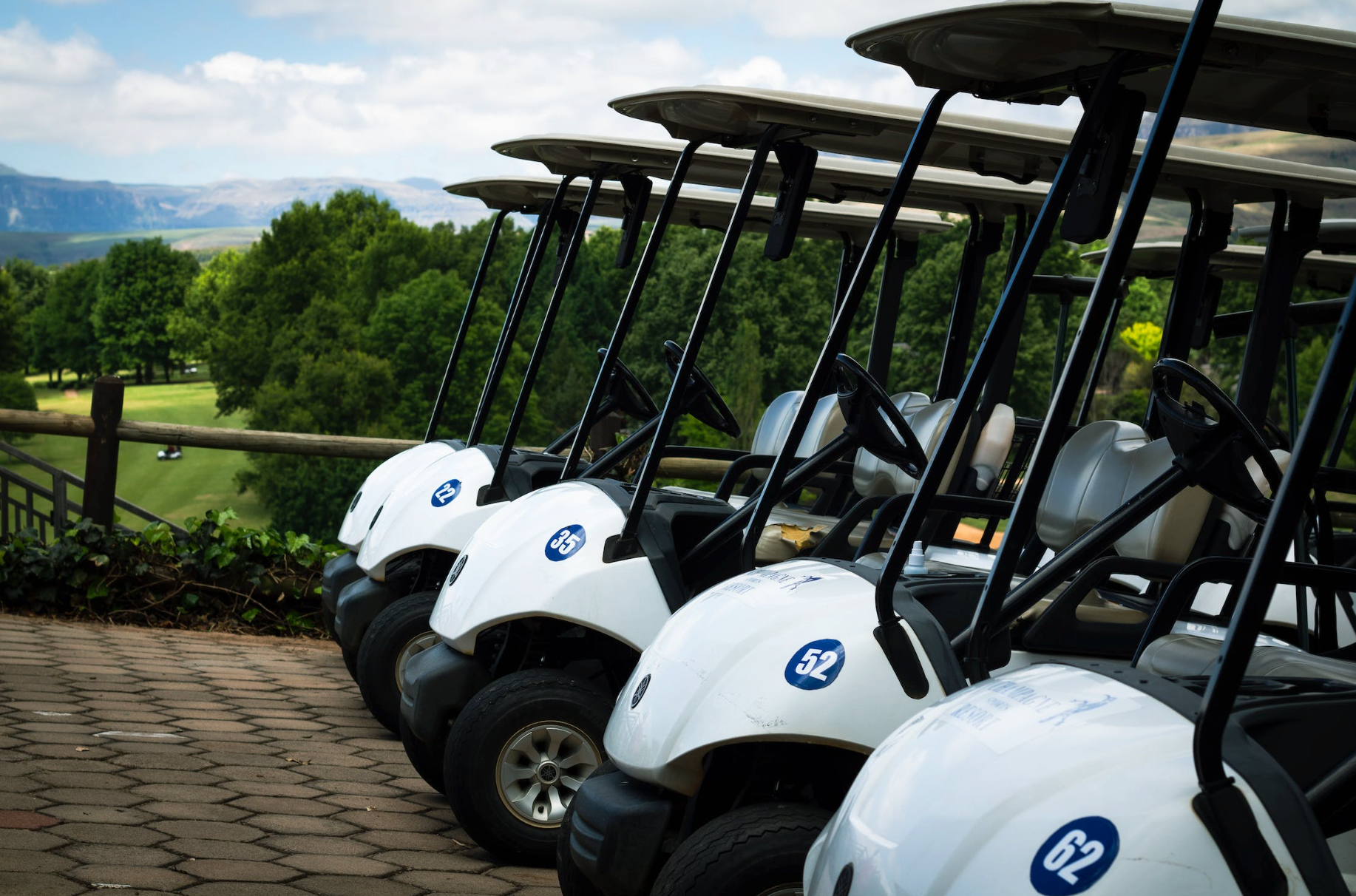 A row of golf carts are parked on the side of a road.
