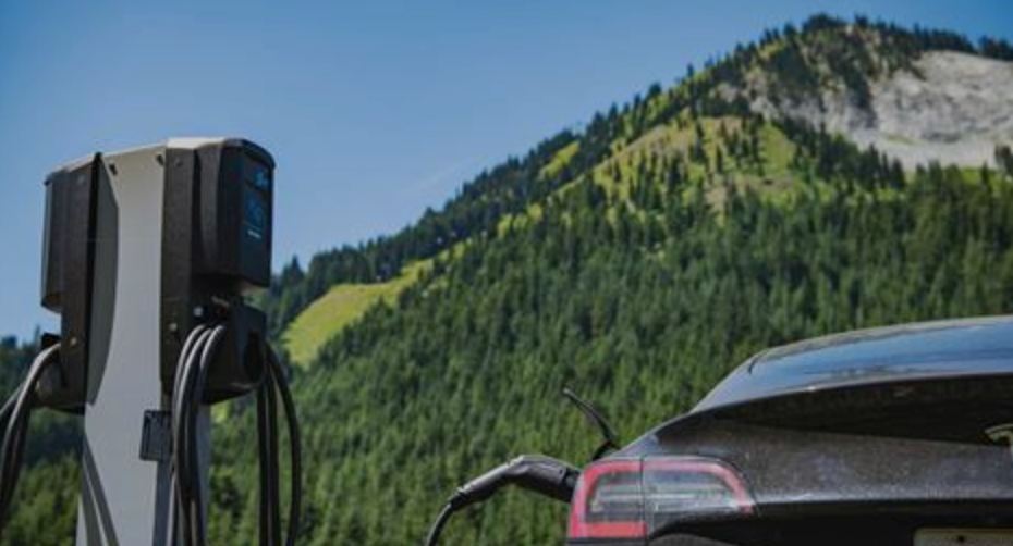A tesla model 3 is being charged at a charging station in the mountains.