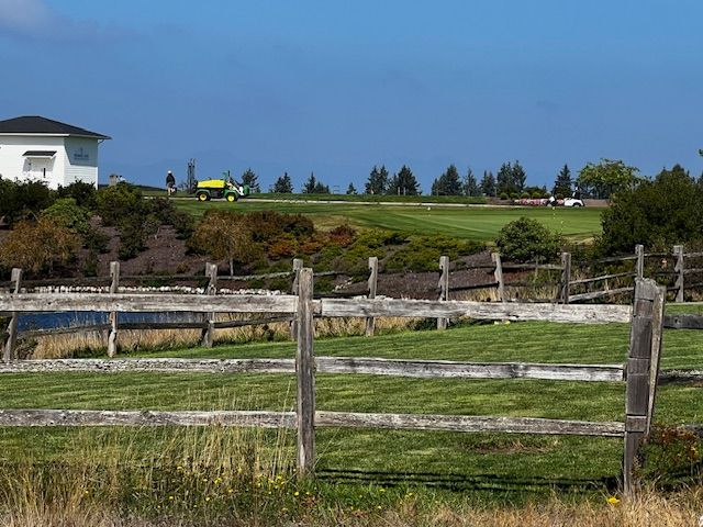 A wooden fence surrounds a grassy field with a house in the background