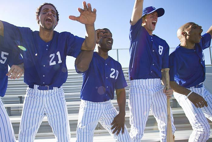 Four baseball players in blue jerseys and white pinstripe pants cheering under a clear sky