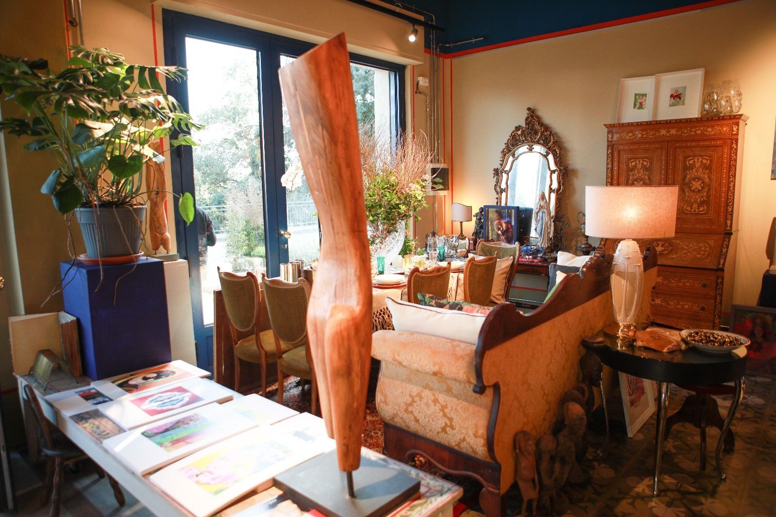 Un soggiorno arredato presenta una scultura astratta in legno, un divano, una lampada alta e una grande pianta vicino a una porta a vetri.