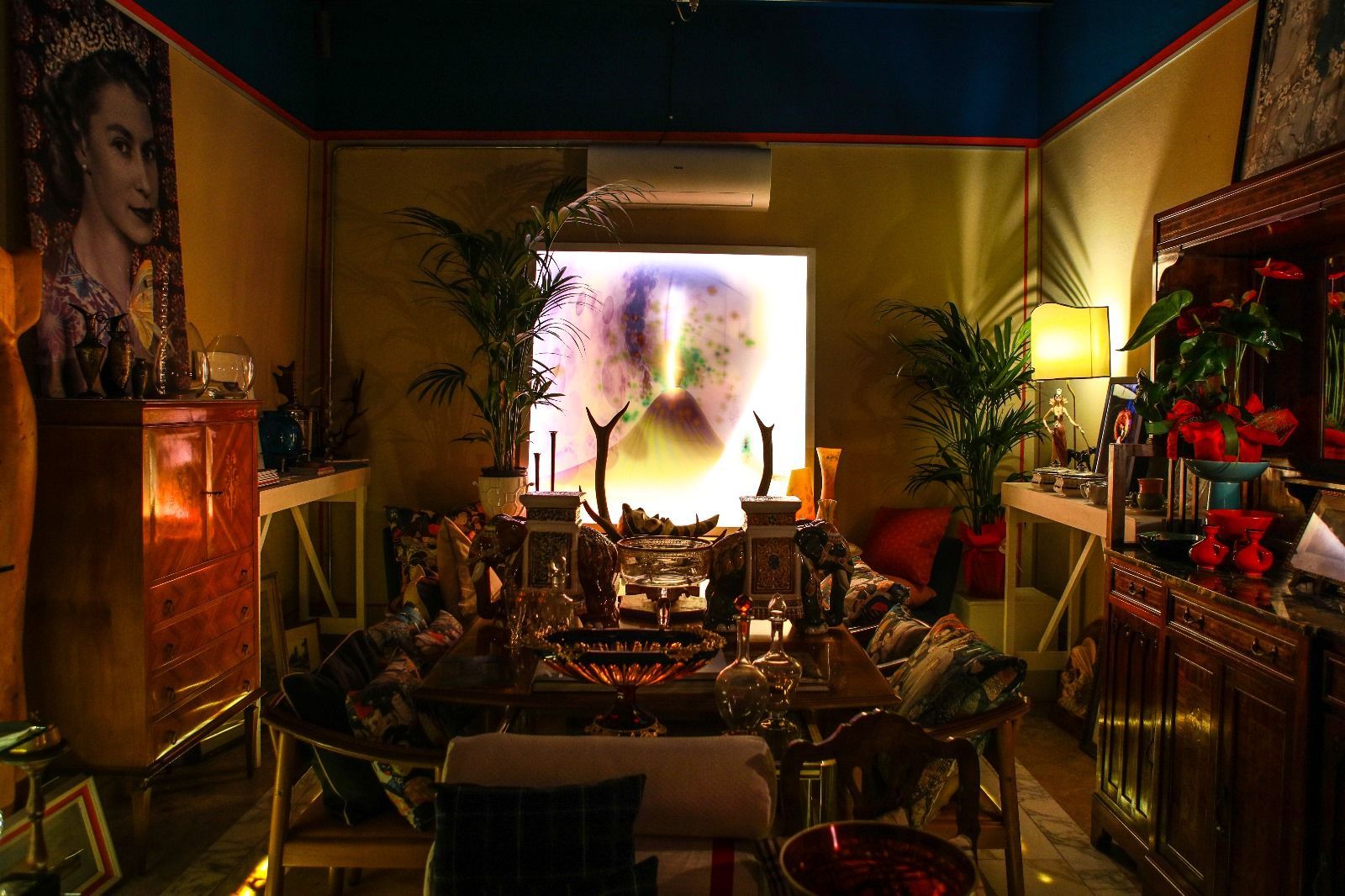 Una stanza in penombra con un tavolo da pranzo centrale, vivaci opere d'arte alle pareti, piante in vaso e una calda illuminazione ambientale.