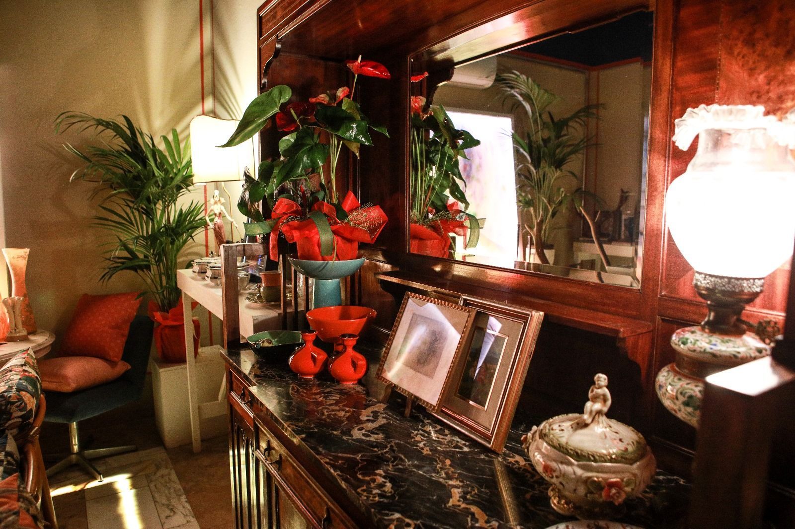 Un interno scarsamente illuminato, caratterizzato da una credenza antica con piano in marmo, lampade, una pianta e una fotografia incorniciata.