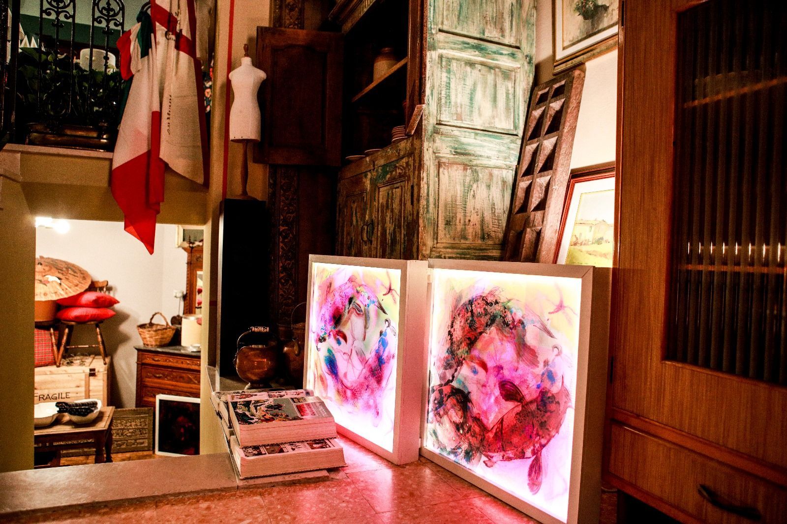 In una stanza rustica ed eclettica, due teche artistiche illuminate, decorate con colorati disegni floreali astratti, sono appoggiate su un bancone.