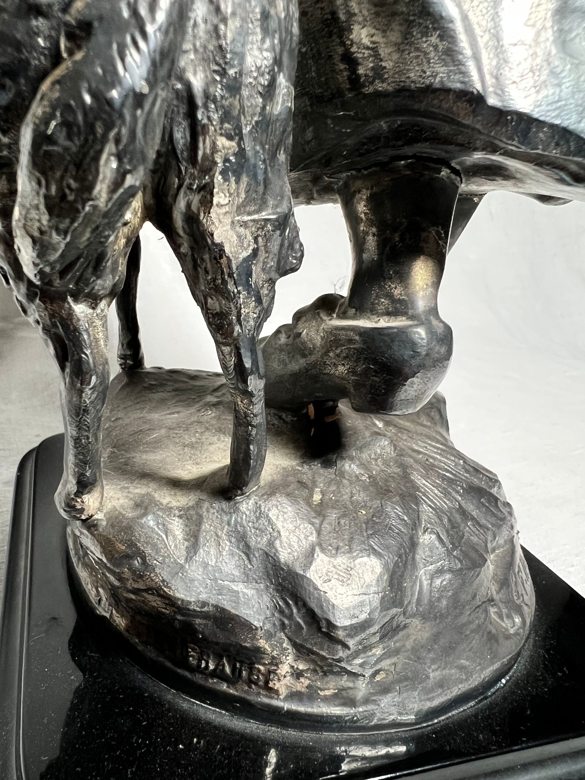 Primo piano di una scultura metallica scura che raffigura uno stivale appoggiato su una base rocciosa, con la scritta