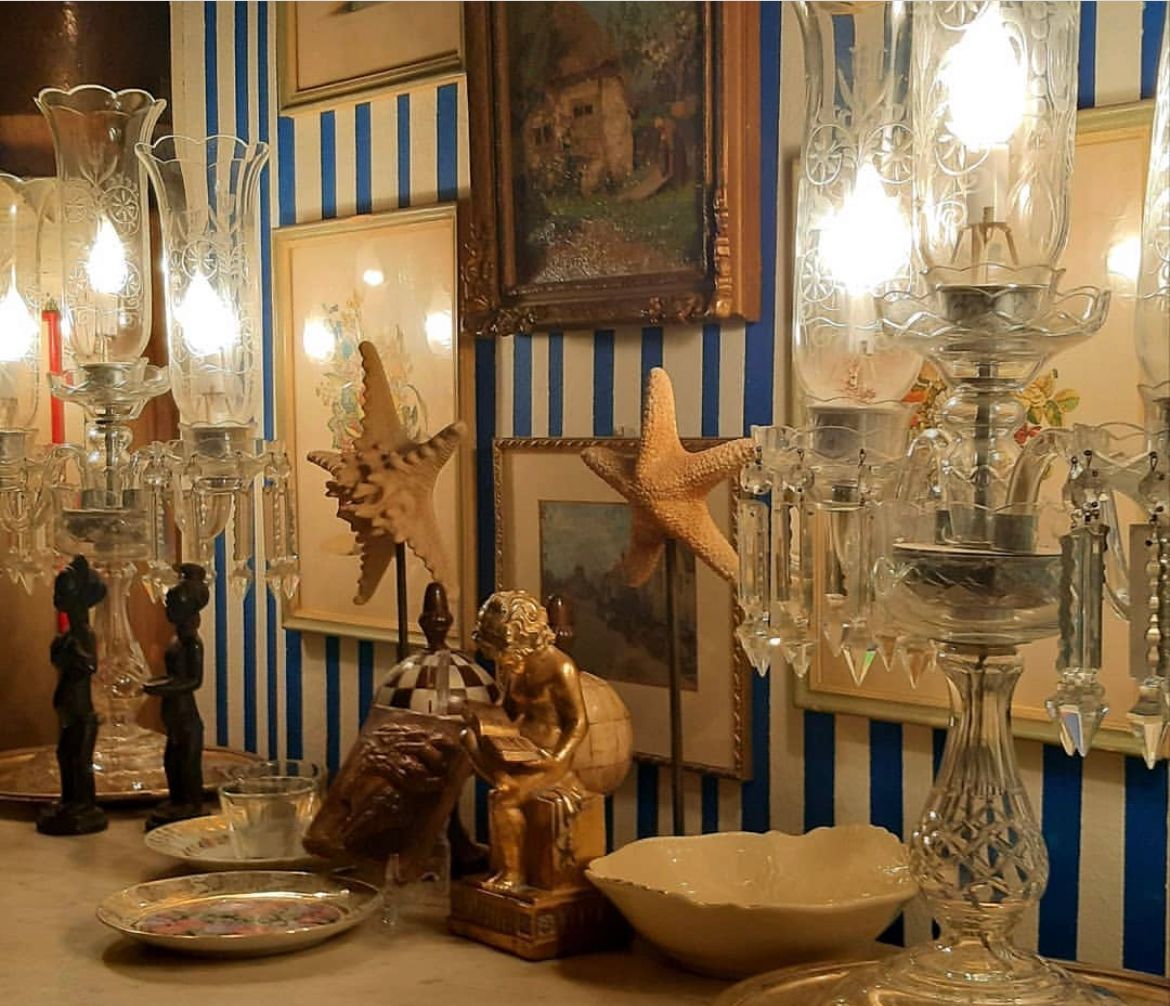 Un tavolo decorato con candelabri di cristallo, decorazioni a forma di stella marina, una piccola statua e quadri incorniciati su uno sfondo a strisce blu.