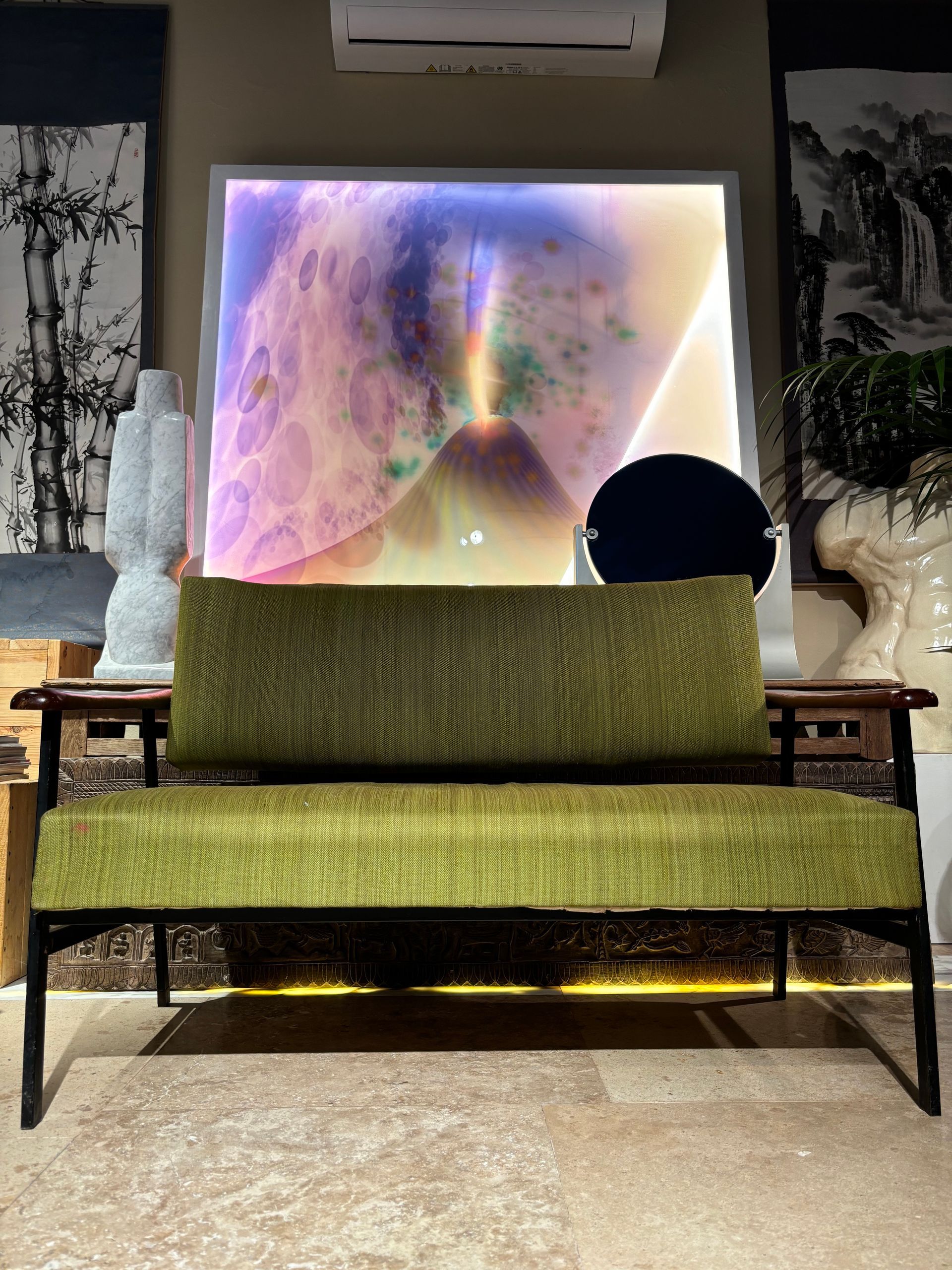 Un divanetto verde lime in stile moderno di metà secolo, con struttura nera, è posizionato di fronte a un'opera d'arte astratta retroilluminata.