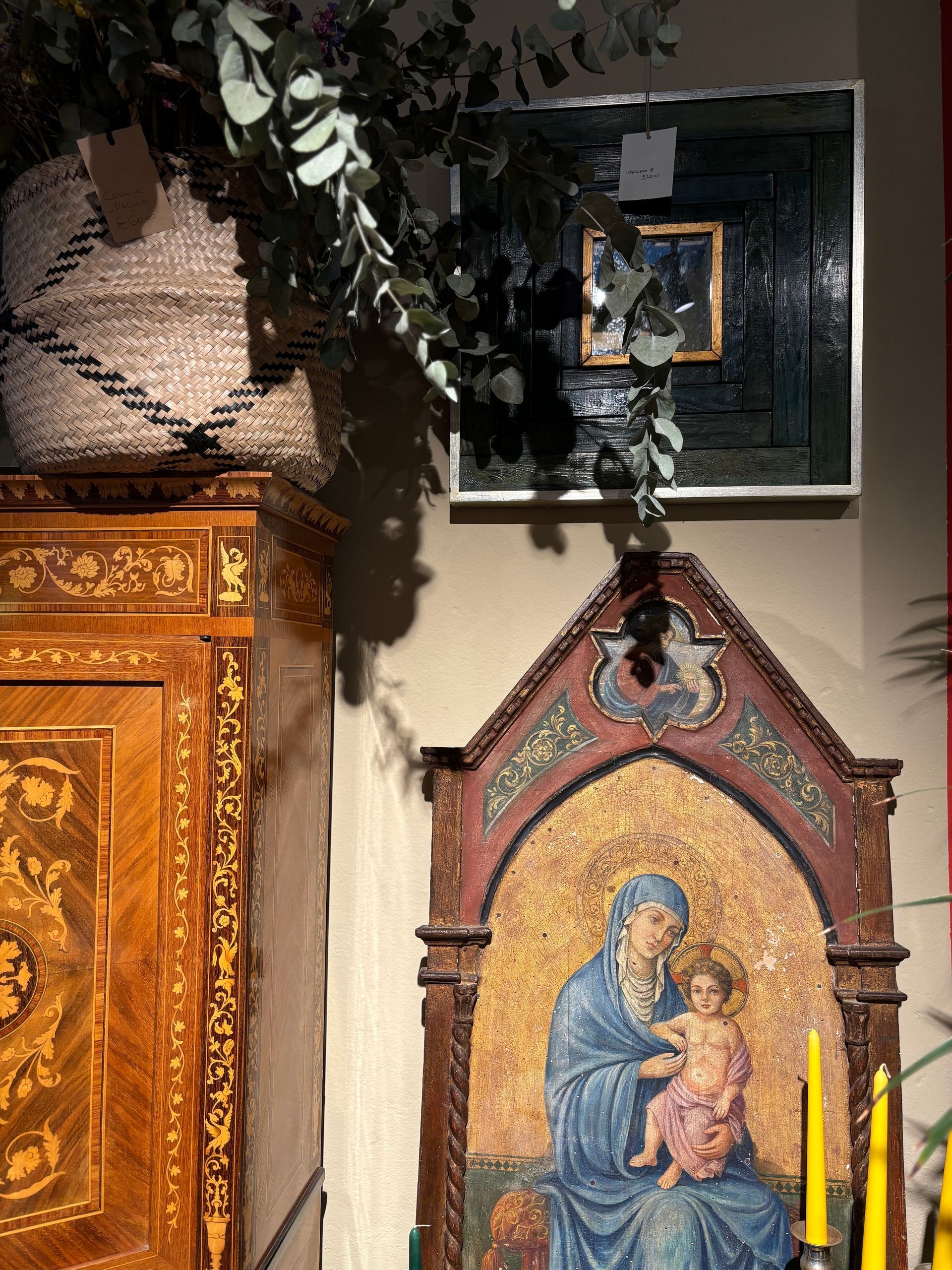 Un antico mobile in legno accanto a un'icona religiosa raffigurante una madre con un bambino, con sopra un cesto di eucalipto.