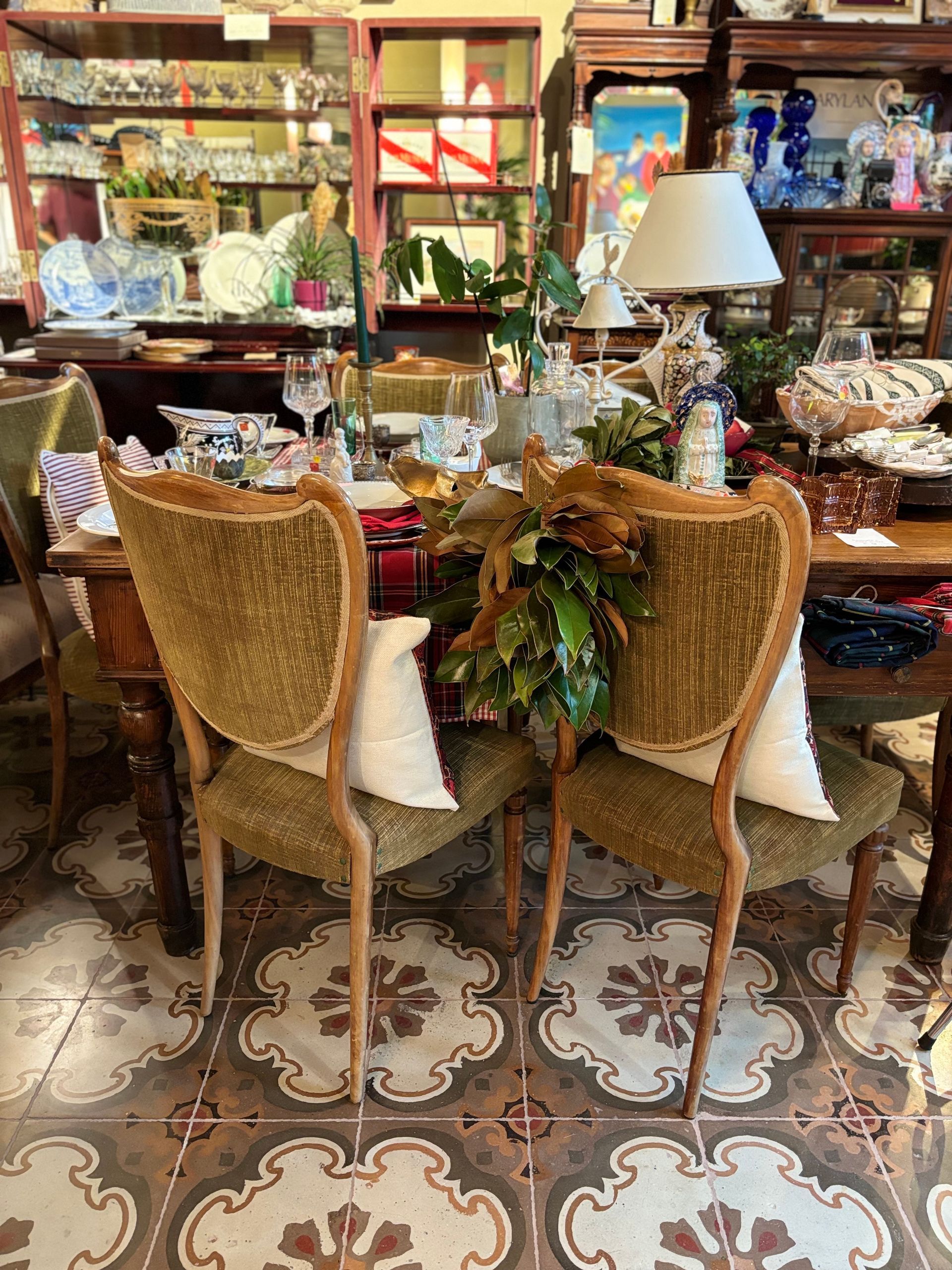 In una stanza con pavimento piastrellato a motivi geometrici e mobili antichi, due sedie da pranzo con finitura dorata sono disposte di fronte a un tavolo decorato.