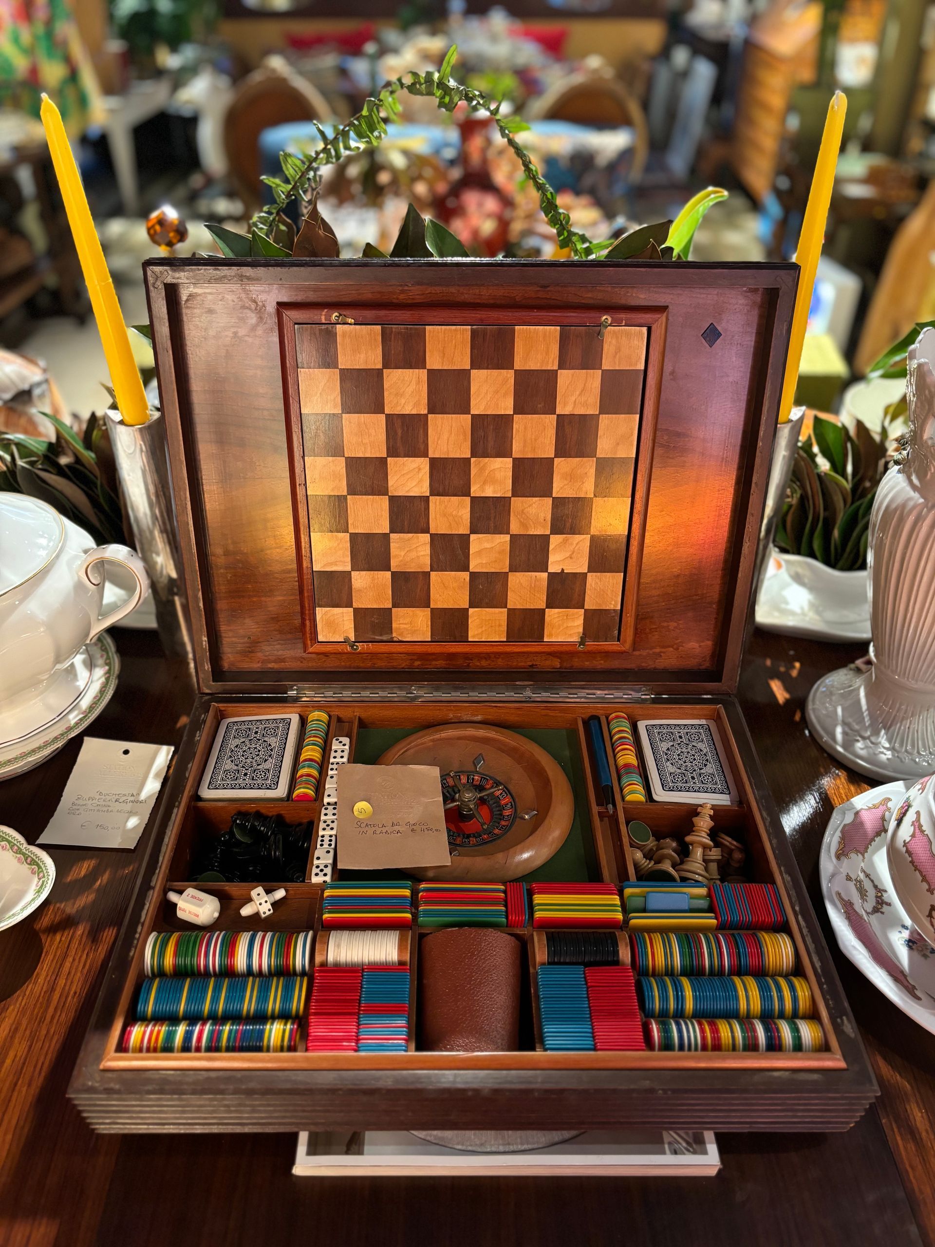 Un set da gioco in legno aperto, completo di coperchio con scacchiera, mazzi di carte e fiches da poker colorate riposte all'interno.