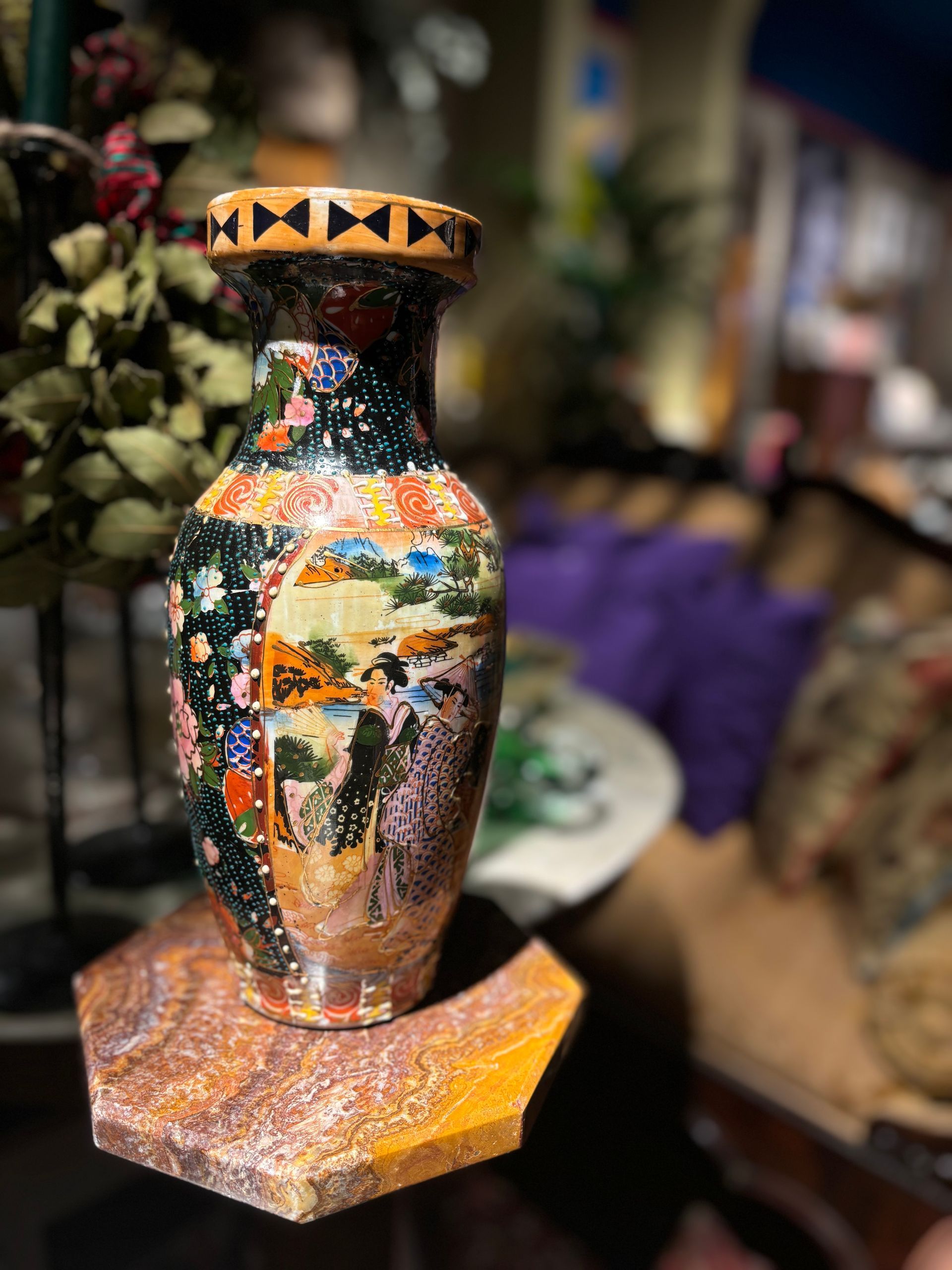 Un vaso decorato con motivi paesaggistici e figurativi in stile giapponese, poggiato su un piedistallo ottagonale in pietra, all'interno di una stanza.