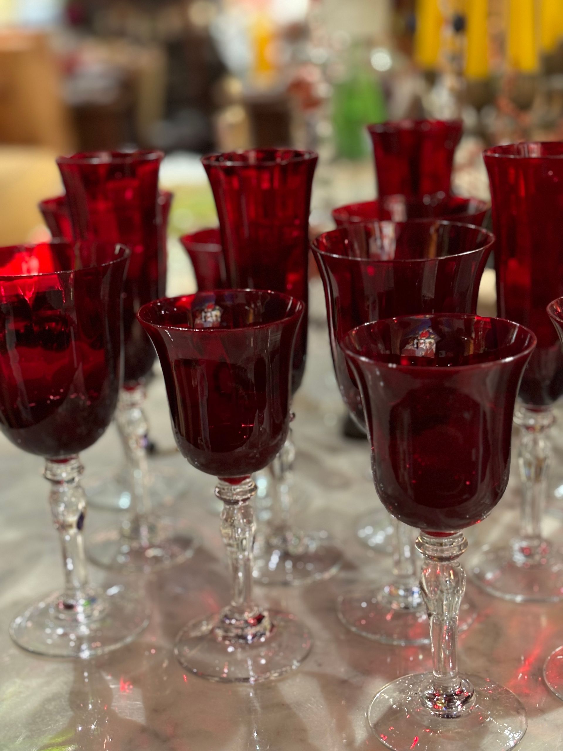 Primo piano di diversi calici di vetro rosso con stelo trasparente, disposti su una superficie.