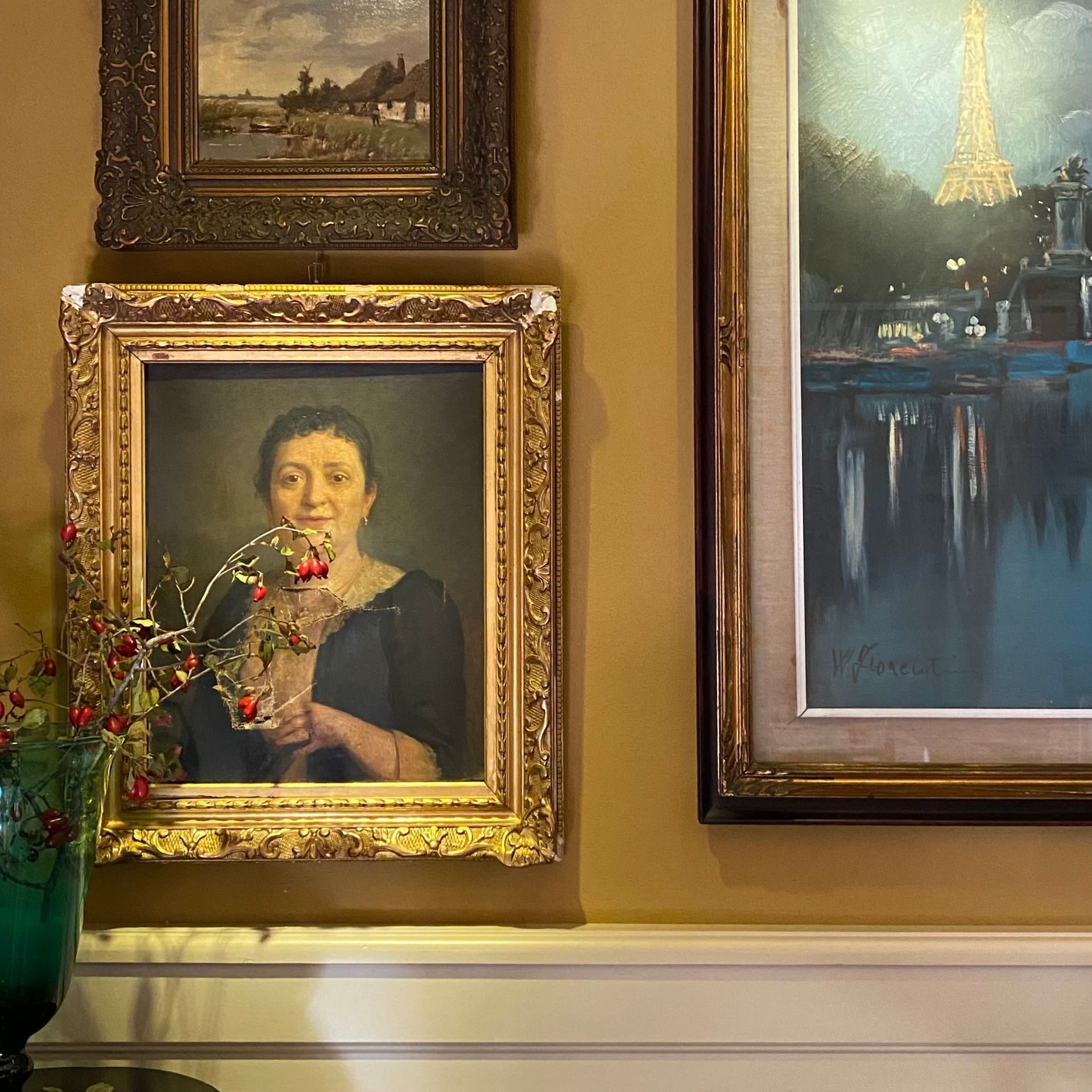 Una parete della galleria presenta un ritratto a olio in una cornice dorata riccamente decorata, un piccolo dipinto paesaggistico e una scena di Parigi.