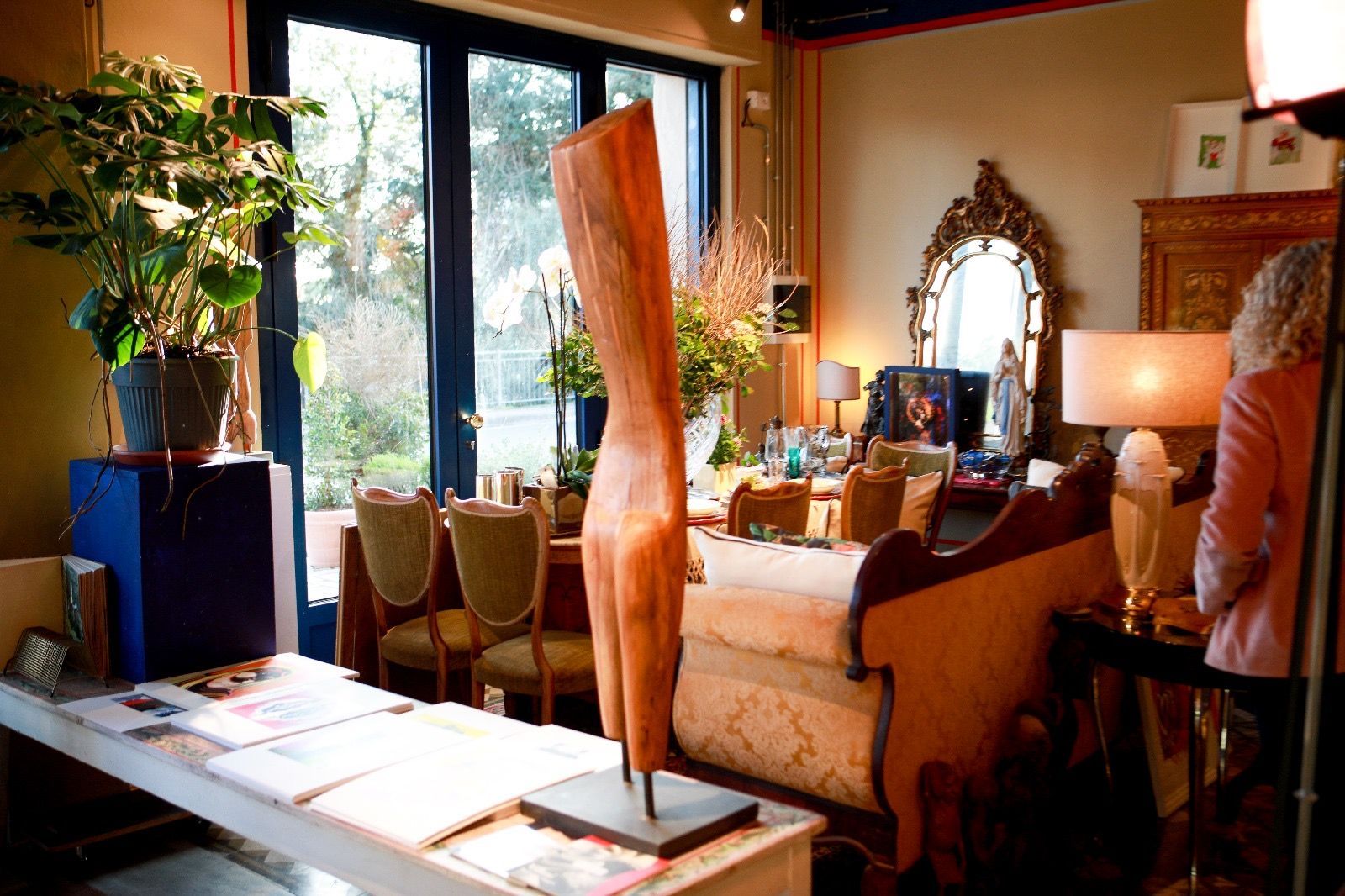 Interno di una stanza con una grande scultura in legno in primo piano, sedie da pranzo, un divano e una grande finestra.
