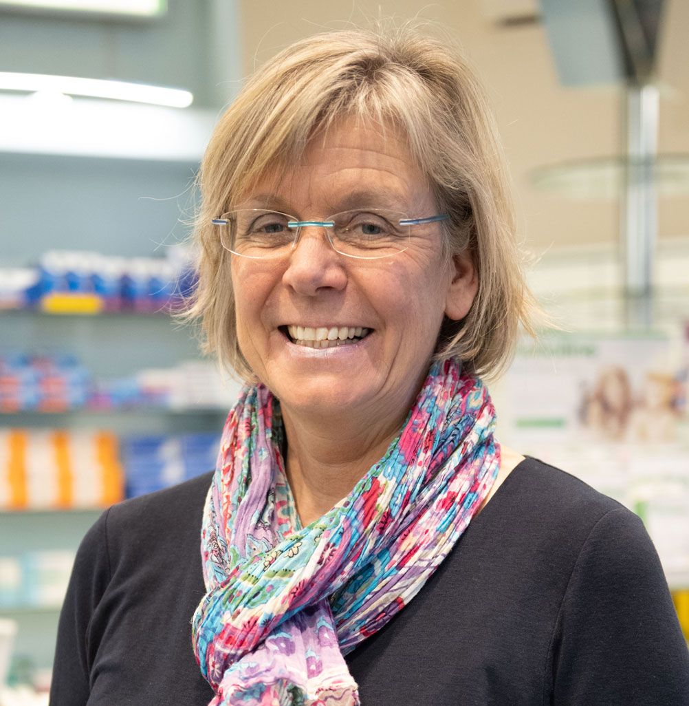 Eine Frau mit Brille und Kopftuch lächelt in einer Apotheke.