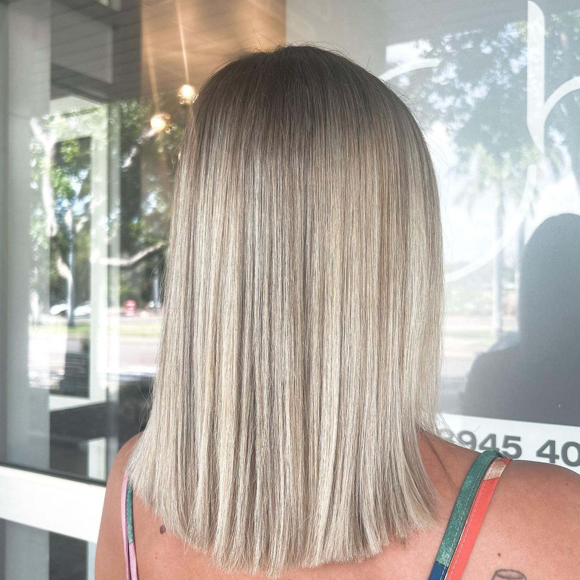 A Woman With Long Blonde Hair Is Standing In Front Of A Wall — Carlee Hair Design In Anula, NT