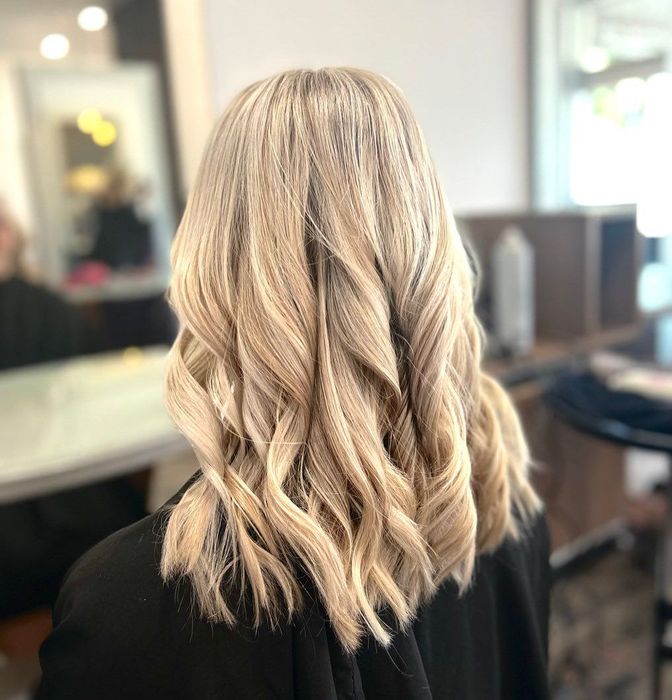A woman with blonde hair that has been curled is sitting in a salon chair — Carlee Hair Design In Anula, NT
