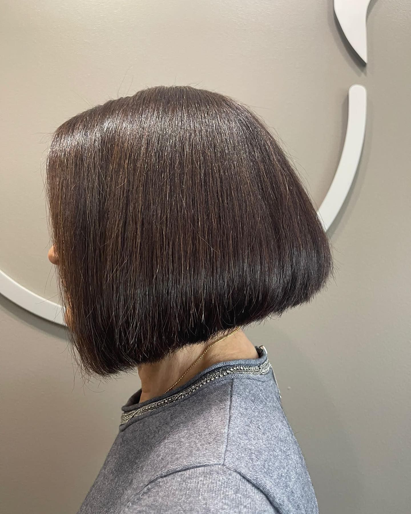 A woman with short dark straight hair is standing in front of a wall — Carlee Hair Design In Anula, NT