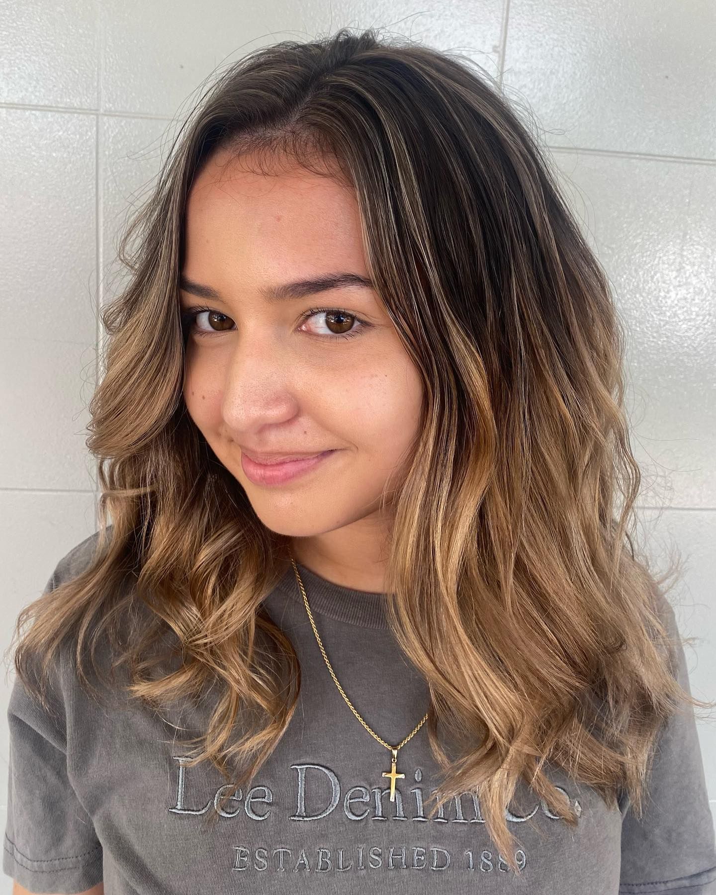 Smiling Person with Wavy Highlighted Hair Wearing a Gray Shirt — Carlee Hair Design In Anula, NT