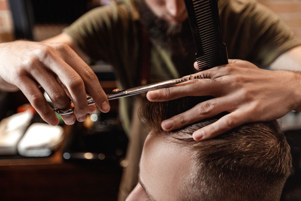 A Man Is Getting His Hair Cut By A Barber In A Barber Shop — Carlee Hair Design In Anula, NT