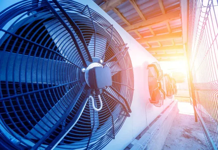 Industrial cooling fans beside a white train in bright sunlight at a rail platform