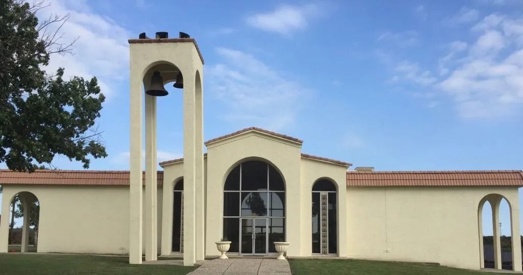 Beige stucco building with bell tower, arched windows, red tile roof, and blue sky.