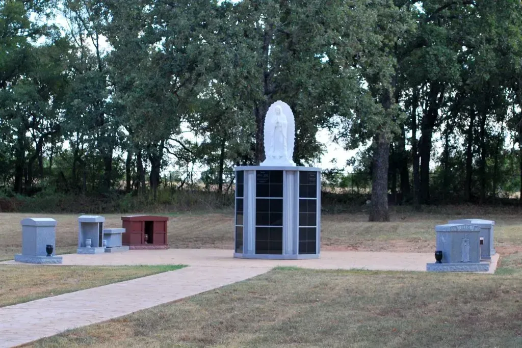 A stone monument with a statue of a figure atop a central pillar, surrounded by smaller memorials in a grassy area.