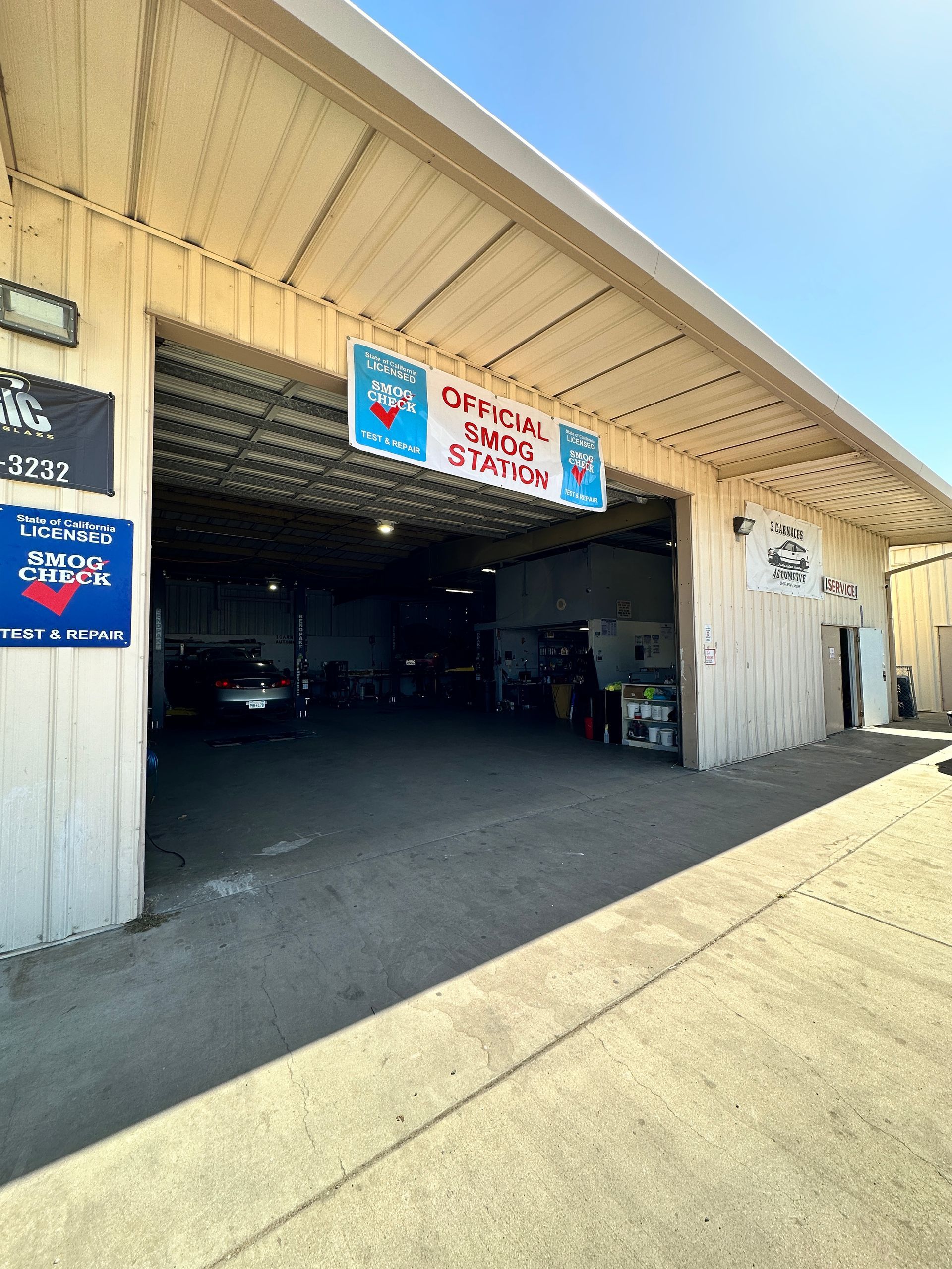 Exterior of a mechanic shop with an open garage bay, a sign, and the Texas flag.
