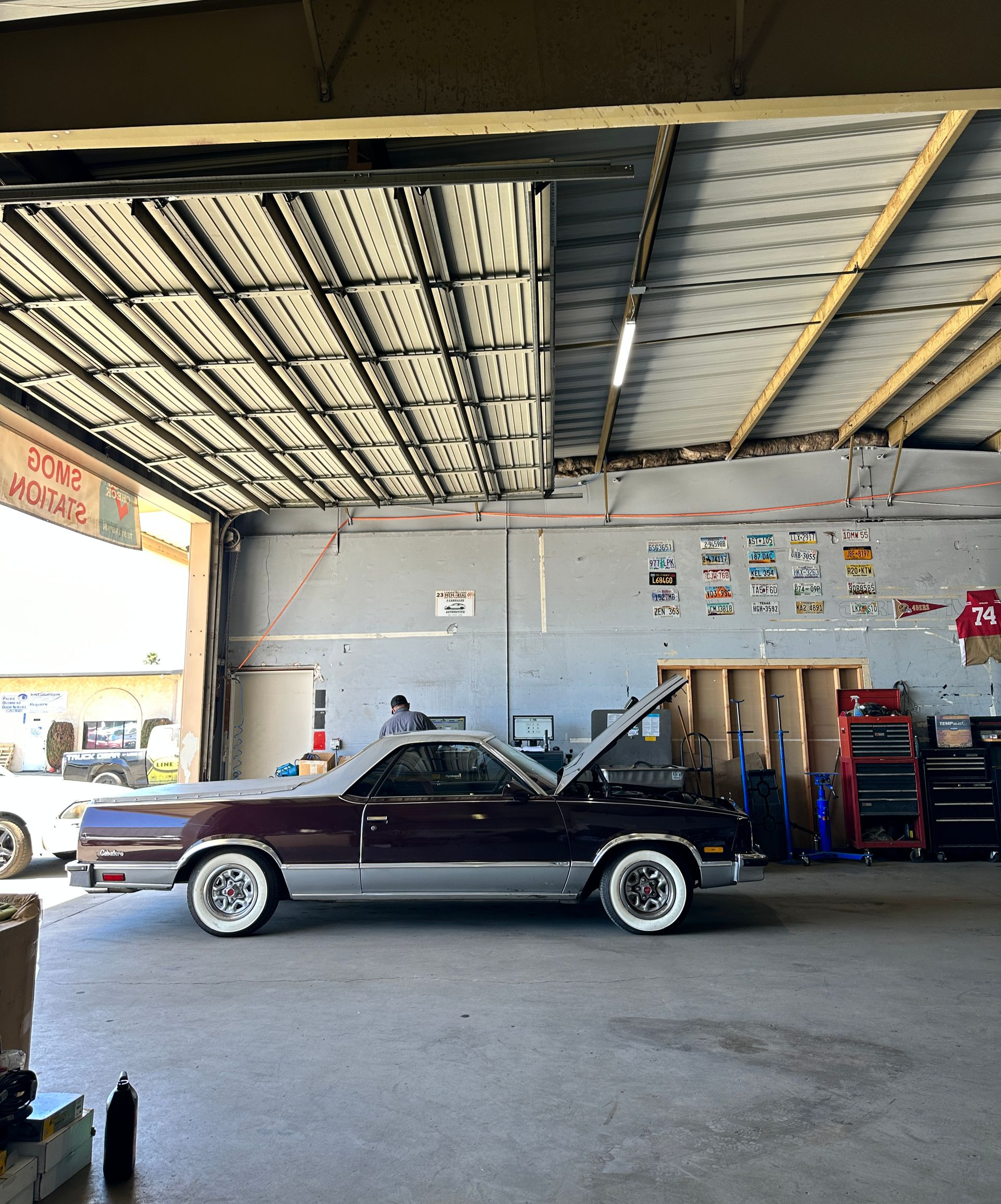Burgundy and silver El Camino in a garage with its hood open.