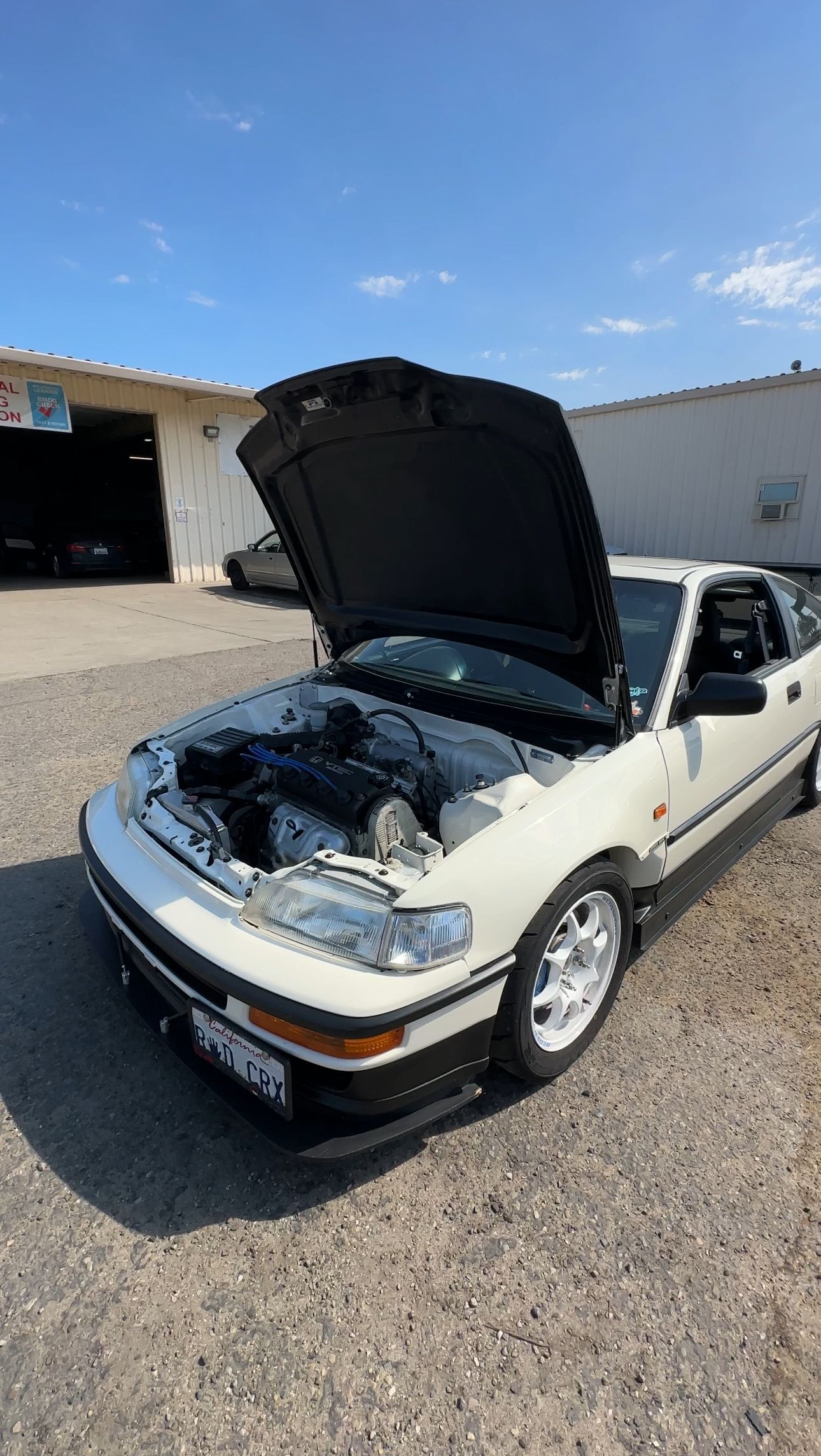 White Honda CRX with hood open, parked outside a building on a sunny day.