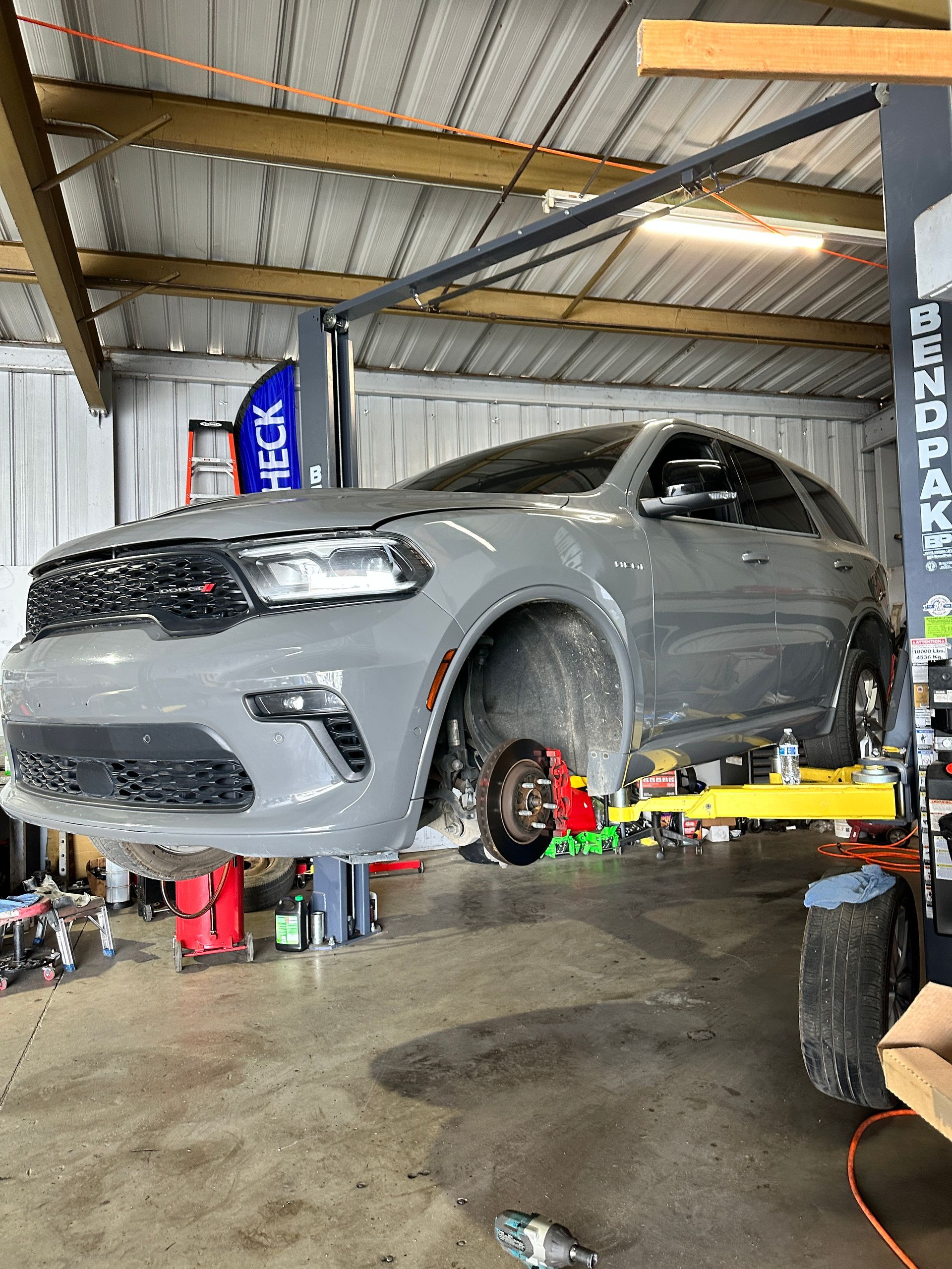 Gray Dodge Durango SUV lifted on a car hoist in a garage; one wheel is removed.
