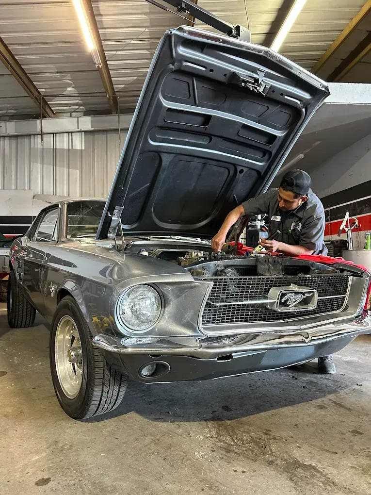 Man working on gray classic Ford Mustang in a garage. Hood is open.