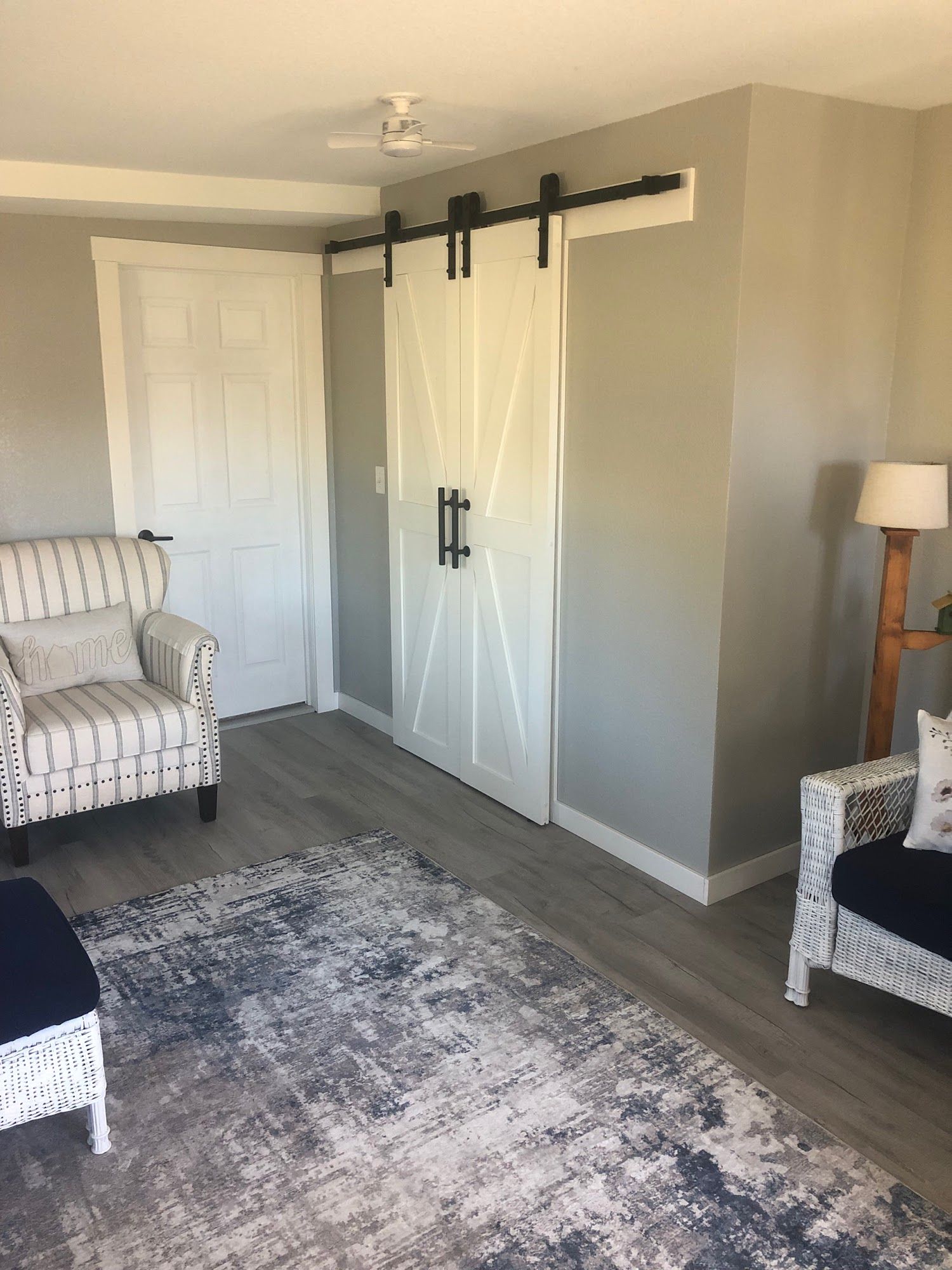 A room with gray walls, a sliding barn door, two white wicker chairs, and a blue and gray rug.