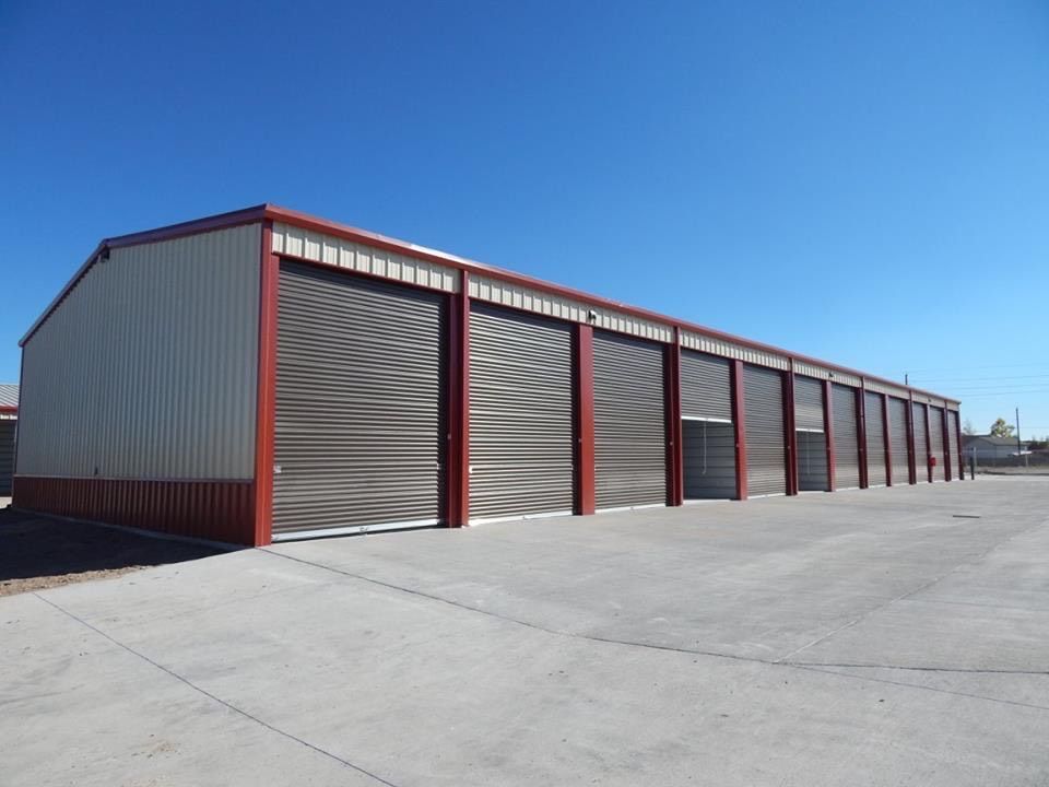 Red and gray industrial metal building with multiple roll-up garage doors on a concrete lot under blue sky