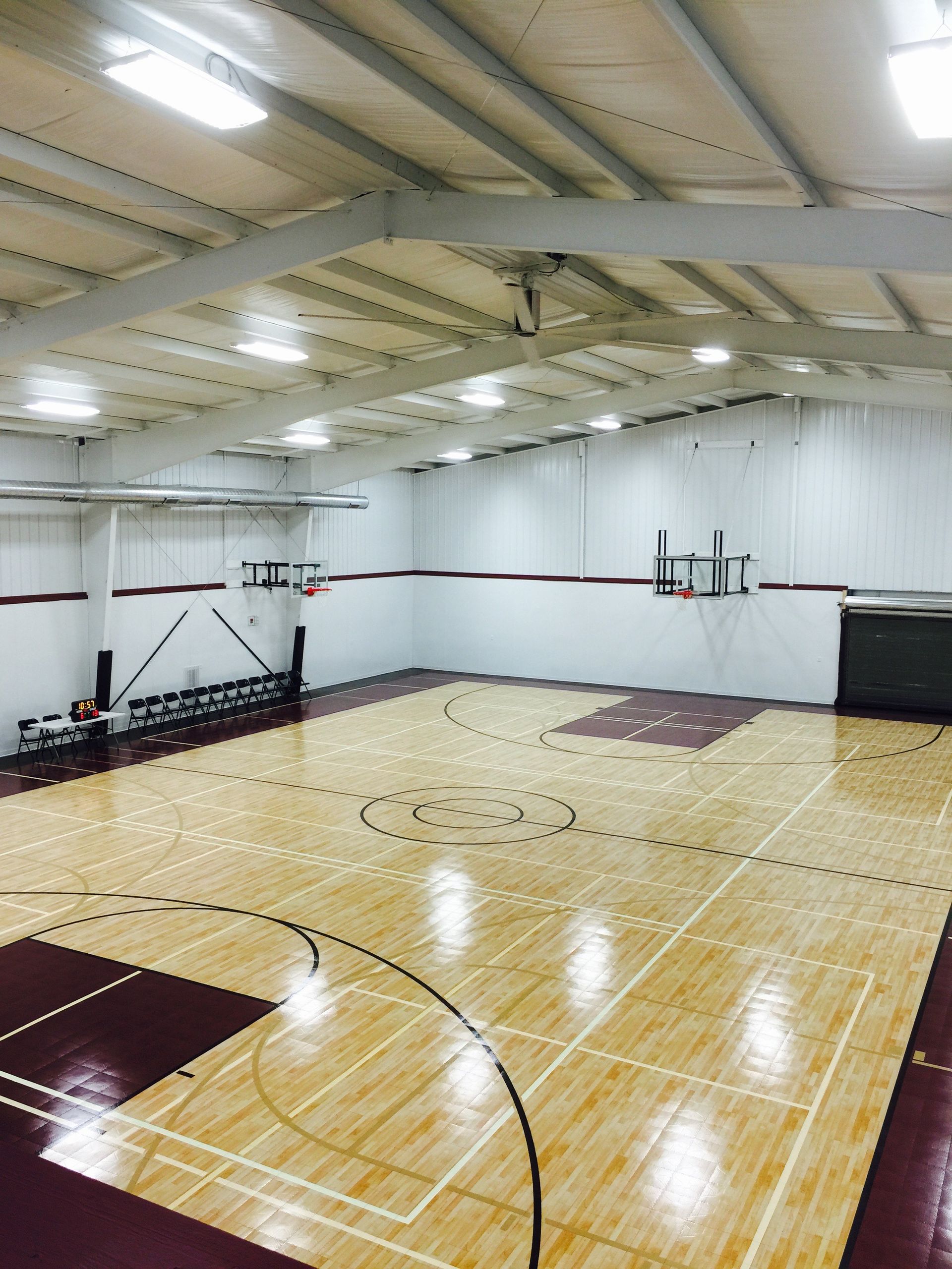 Empty indoor basketball court with polished wood floor, white walls, and overhead lights