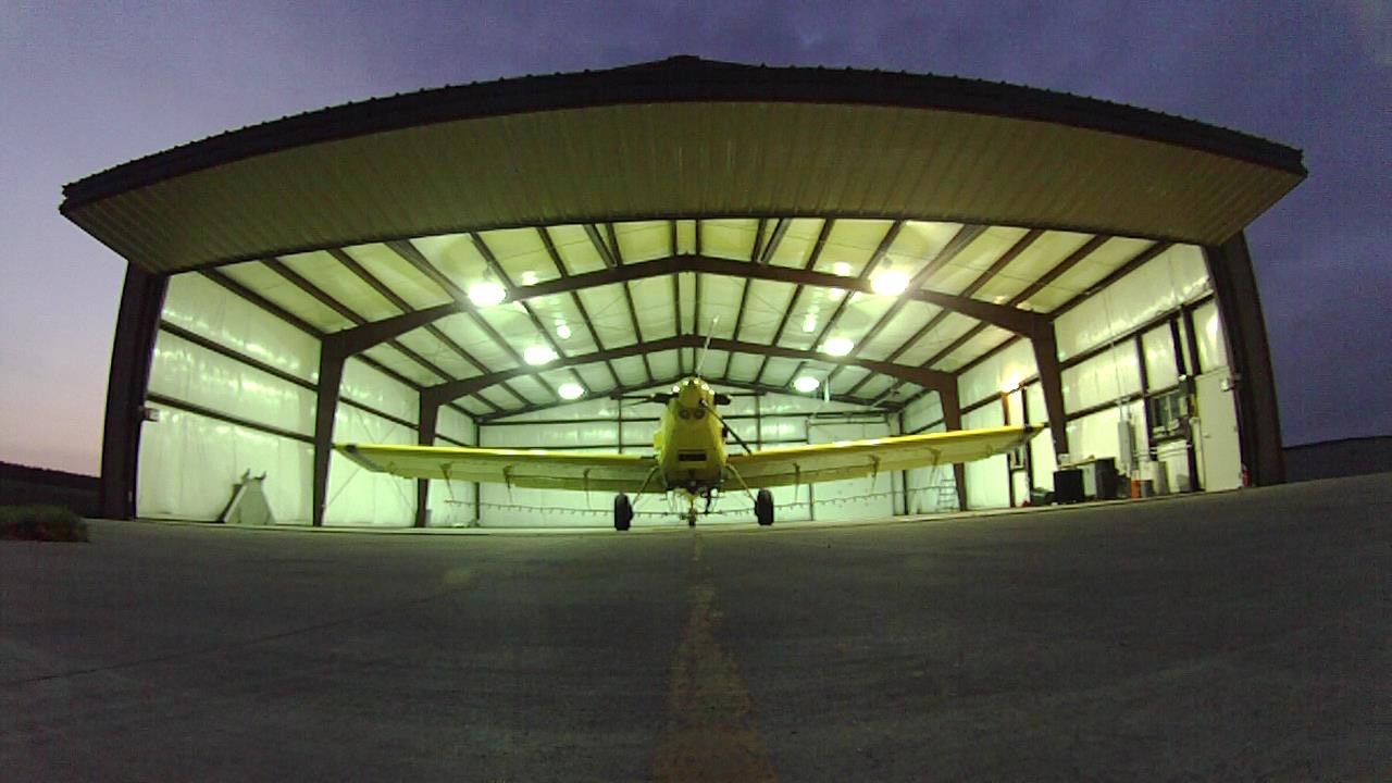 Small airplane in a brightly lit hangar, viewed from the open doorway at dusk.