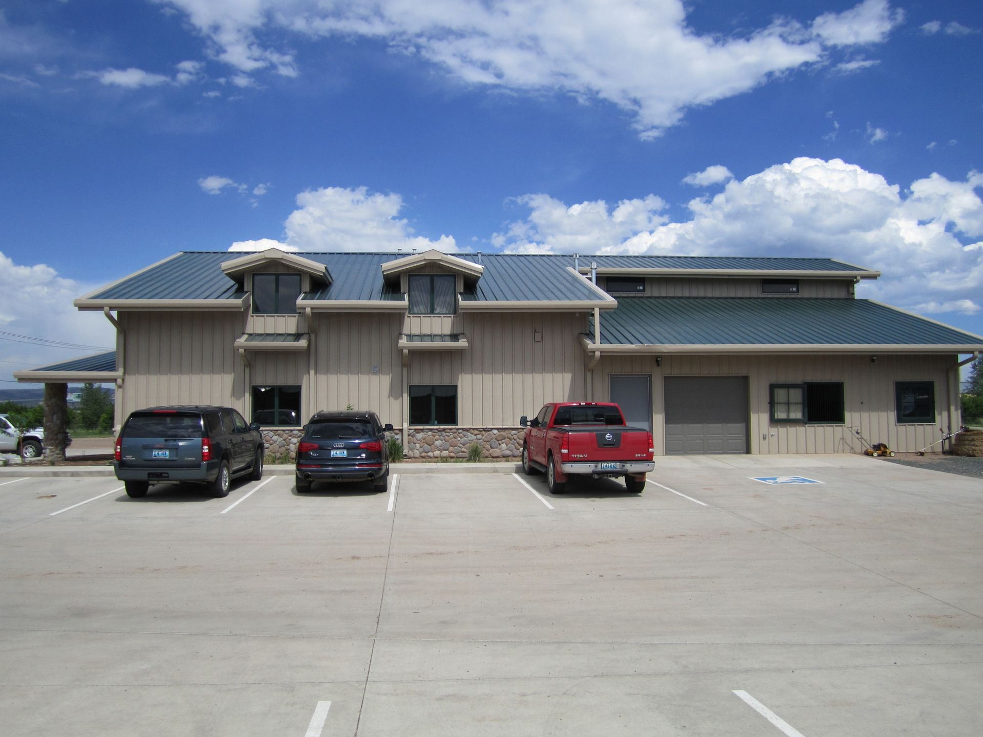 Single-story building with a metal roof and three parked cars in front under a blue sky
