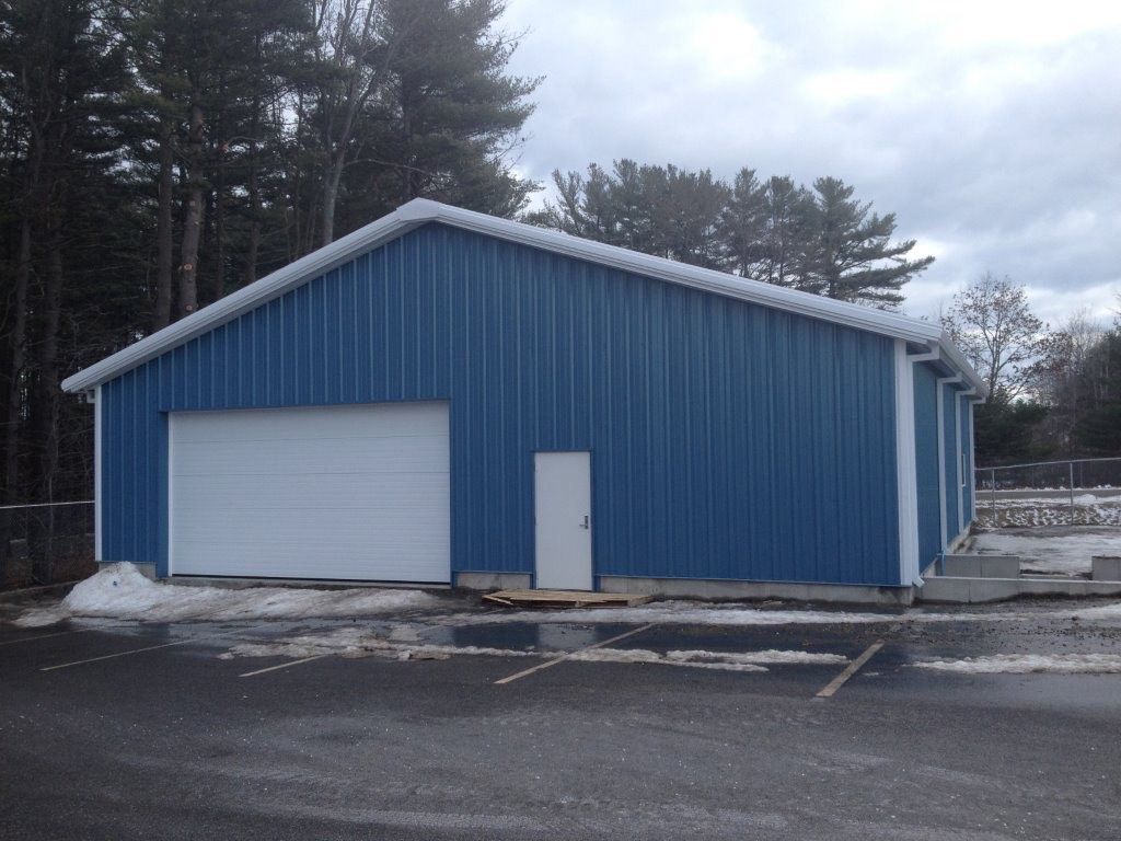 Blue metal warehouse with a white garage door and side door in a snowy lot